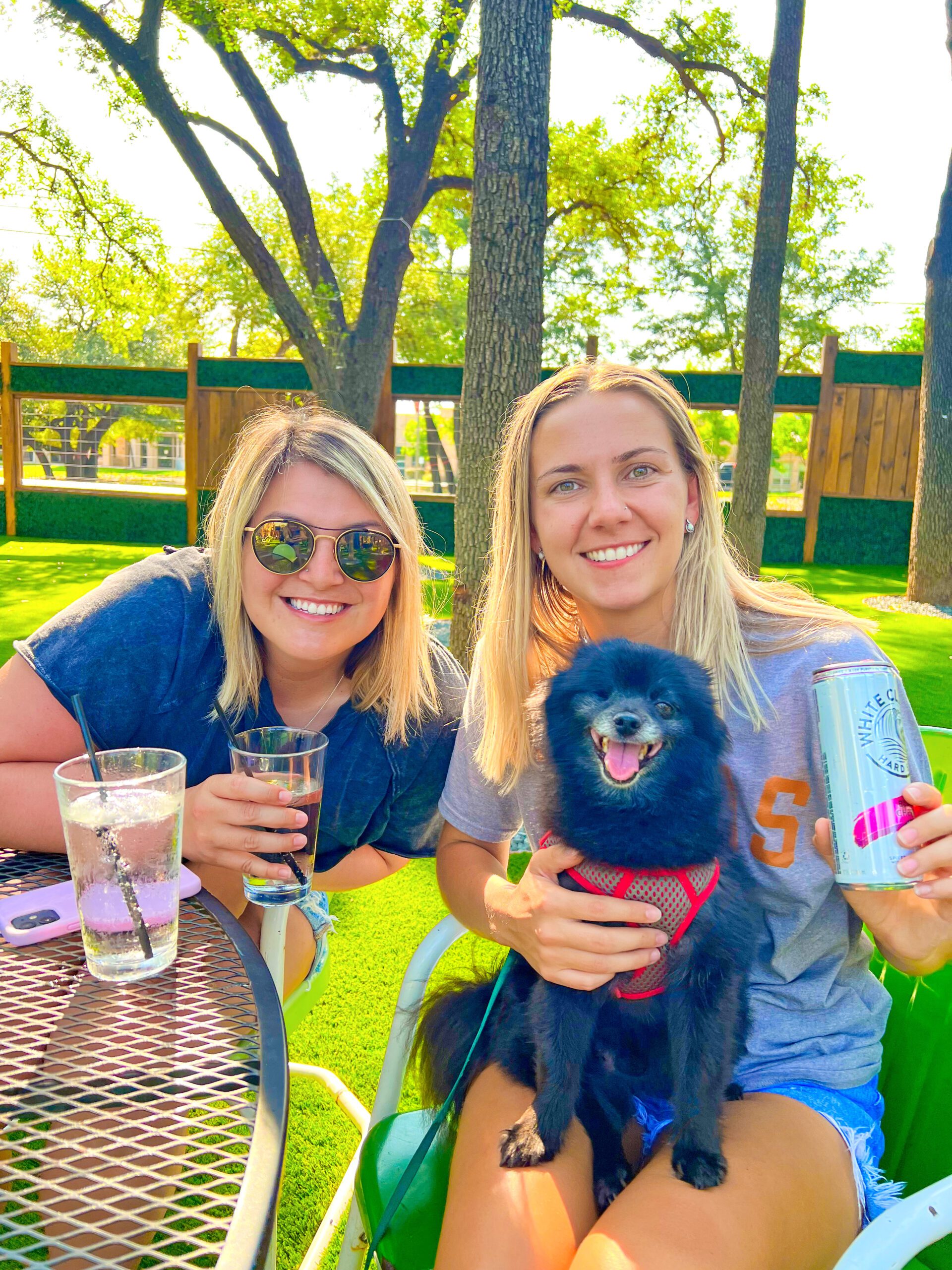 two young women enjoying drinks with dog on the patio